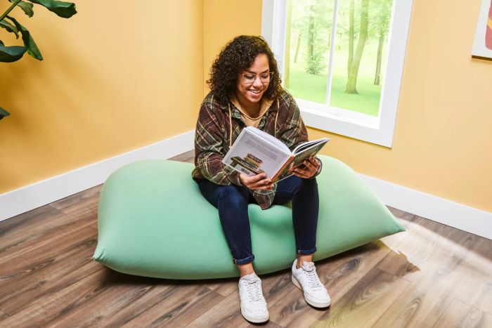 A person sitting on a Yogibo Short Bean Bag Chair, reading a book.