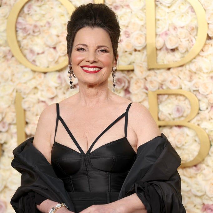 Fran beams in a chic dress and matching jacket, holding a sparkling handbag, against a floral backdrop.
