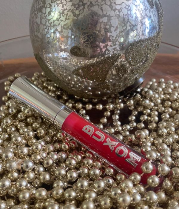 A Buxom lip gloss tube elegantly placed amidst decorative pearls and a shiny metallic ornament.