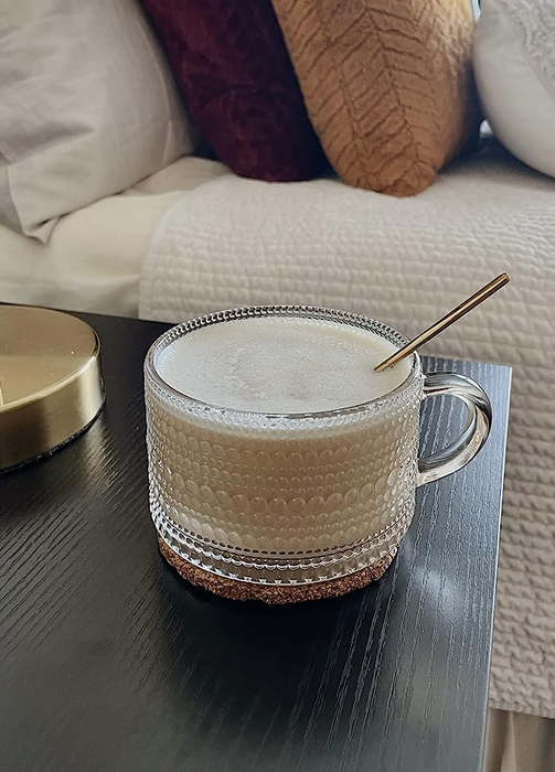 A glass mug with subtle etched line and dot patterns, holding a cup of coffee.