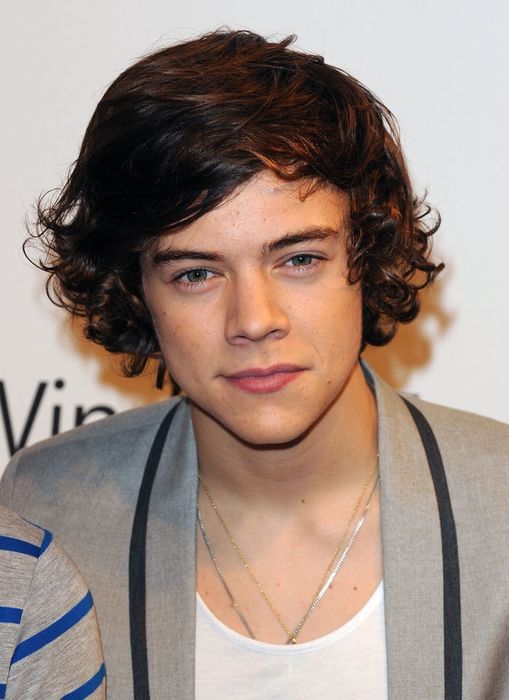 A person with curly hair wearing a gray jacket and white shirt