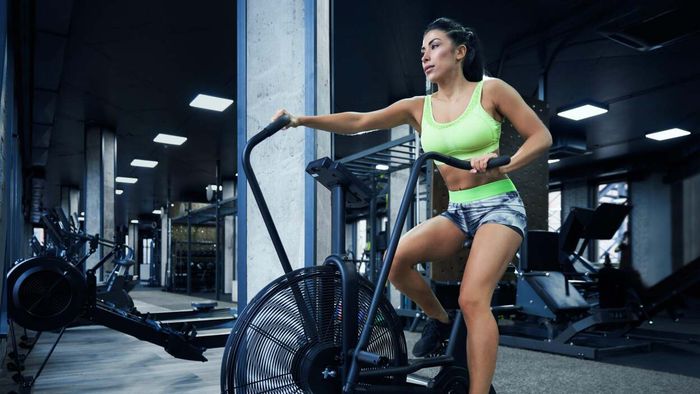 A woman in Spandex workout gear exercises on an elliptical machine in a gym, which is otherwise empty except for workout equipment.