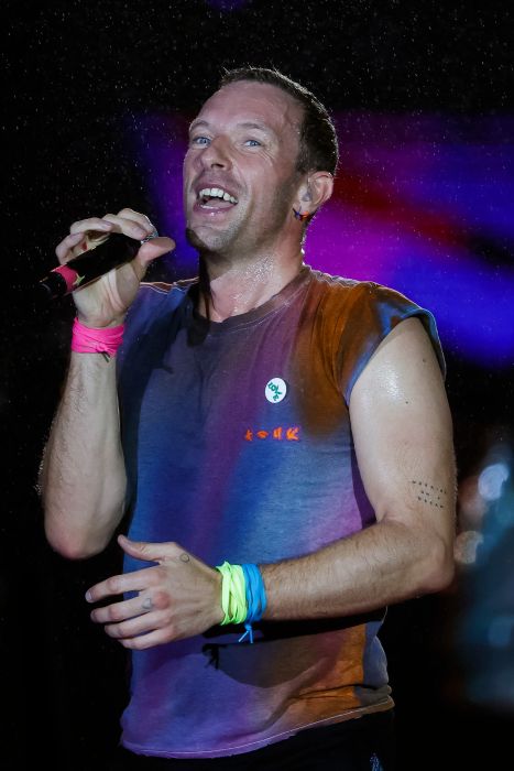 A person passionately sings on stage, sporting a sleeveless top and colorful wristbands, holding a microphone with enthusiasm.