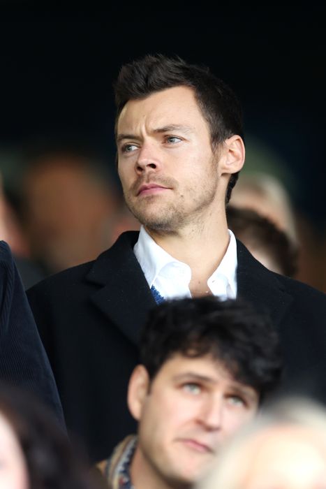 A person dressed in a formal coat and shirt, appearing serious and focused amidst a crowd