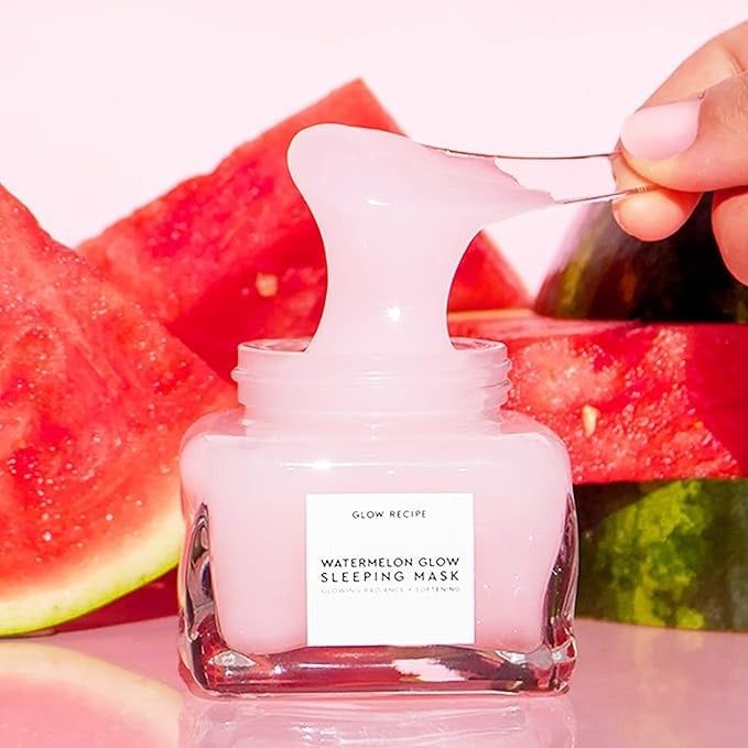 Glow Recipe Watermelon Glow Sleeping Mask shown next to fresh watermelon slices. A hand holds a spoonful of the mask above the open jar