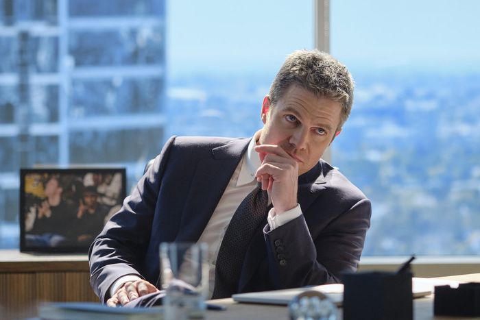 Stephen Amell, dressed in a suit, sits at a desk in a scene from 'Suits: LA'