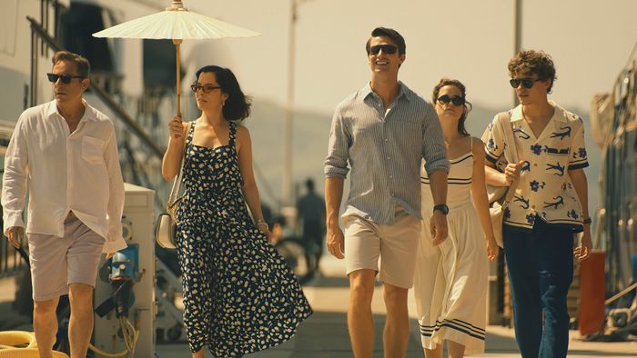 A group of five people stroll along a boardwalk in a scene from 'The White Lotus' Season 3. One woman holds a parasol. They’re dressed in casual summer attire.