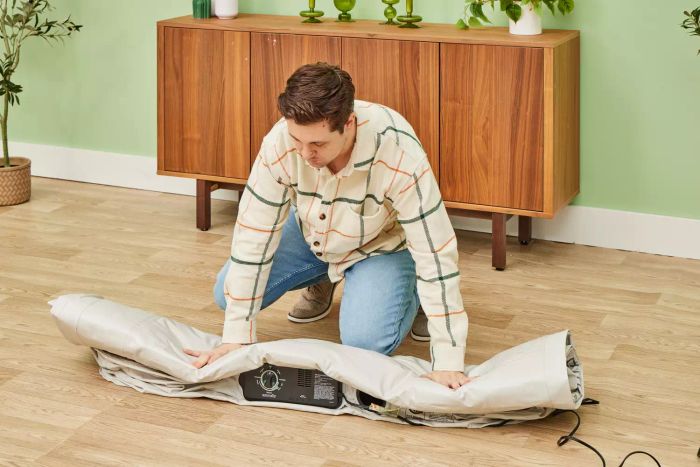 A person is folding the SereneLife Luxury Full-Size Air Mattress with Built-in High-Speed Pump for storage.