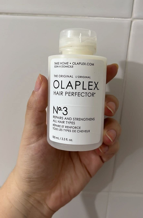 A hand holding a bottle of Olaplex No. 3 Hair Perfector, a treatment designed for hair care