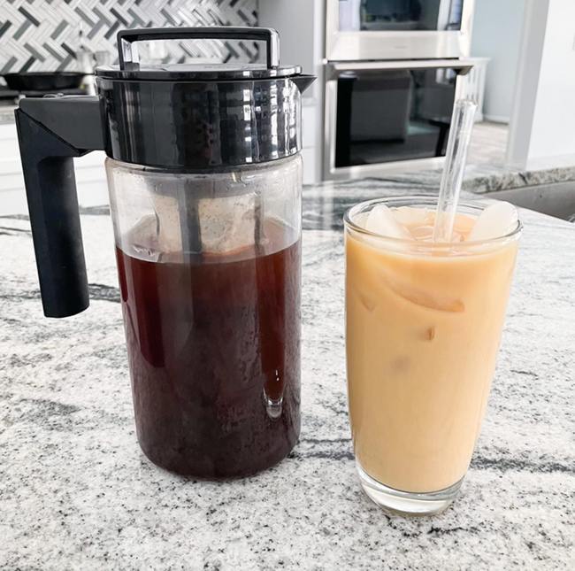 A cold brew coffee pitcher placed next to a glass of iced coffee.