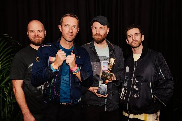 Four individuals gather together, one holding a trophy. They are dressed in casual yet trendy outfits, featuring jackets and graphic tees