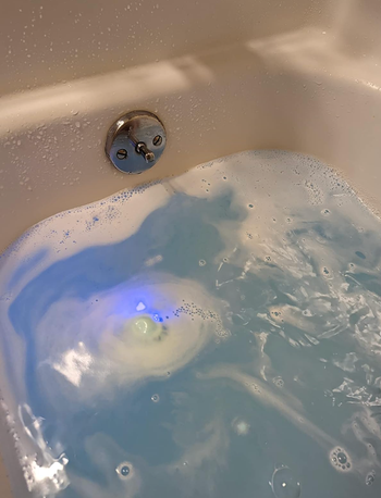 A bath fizz dissolving in water, turning it blue while glowing with an inner light.