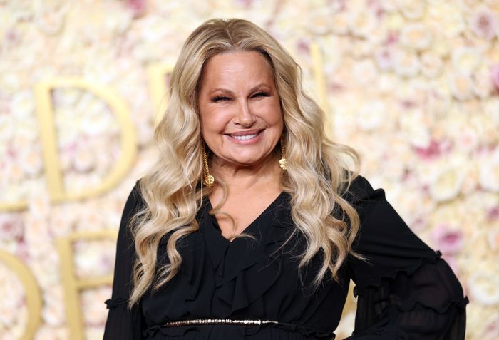 A person in an elegant black dress smiles in front of a floral backdrop at a celebrity event.