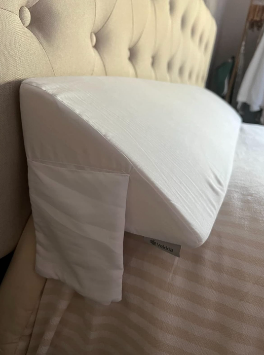 A white, triangle-shaped pillow that stretches across the top of a reviewer’s bed.