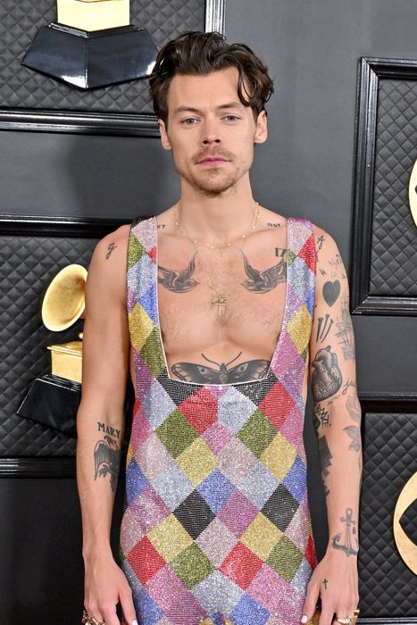A person wearing a glittering, harlequin-patterned jumpsuit with a plunging neckline, posing on the red carpet at an awards event