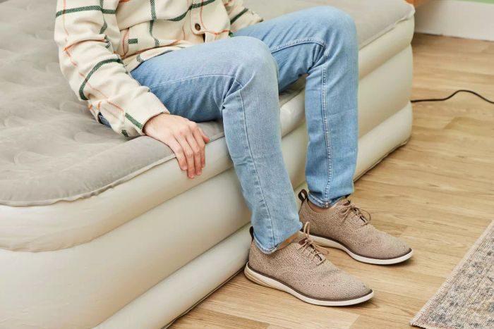 A person is sitting on the SereneLife Luxury Full-Size Air Mattress with Built-in High-Speed Pump.