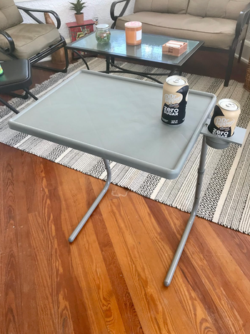 A small gray tray table with two legs, holding a can of coke.