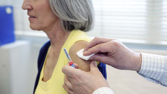 A gray-haired woman has her arm swabbed in preparation for receiving a flu shot.