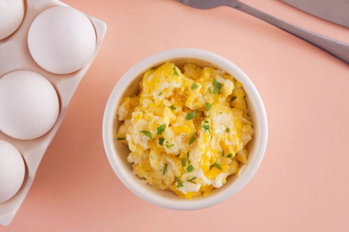 A bowl of scrambled eggs, viewed from above, arranged in a flat lay style with soft, light tones, conveying a conceptual theme