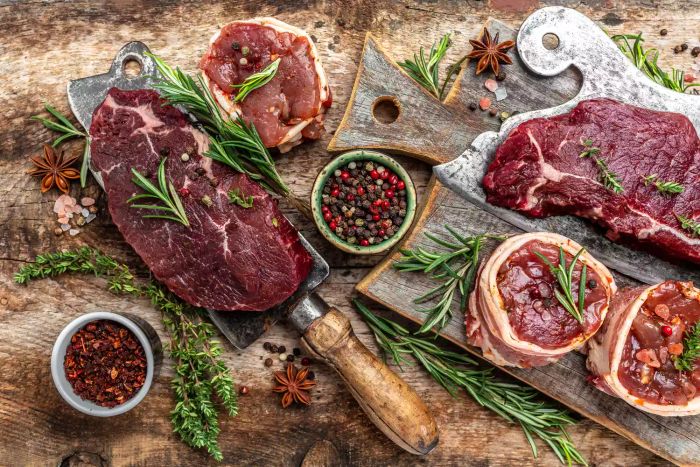 A selection of raw beef steaks ready for grilling, seasoned and placed next to a butcher knife. Top view of a recipe banner.