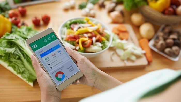 Individual using a calorie tracking app while preparing vegetables.