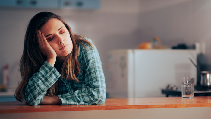 A woman in pajamas standing by her kitchen counter with her eyes closed.
