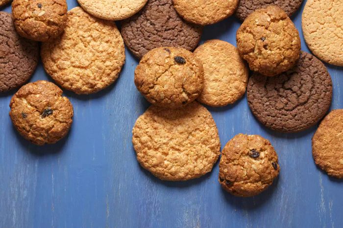 A variety of shortbread and oat cookies with cereals and raisins on a blue wooden surface. A top-down view.