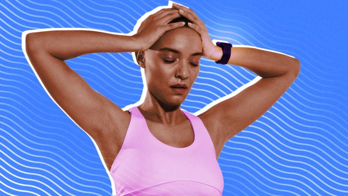 A frustrated woman dressed in workout attire, wearing a fitness tracker, with her hands on her head