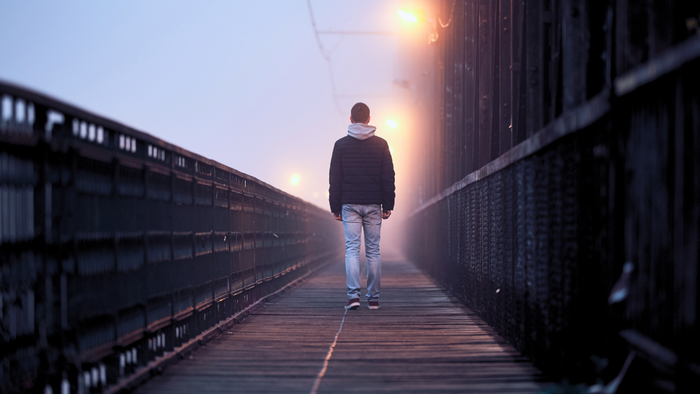 A picture of a man walking on a foggy boardwalk, viewed from behind