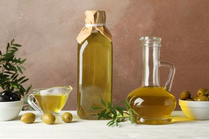 A bottle and jug of olive oil accompanied by olives, set against a brown background with space for text