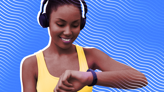 A woman in running attire, wearing headphones, glancing at the smartwatch on her wrist