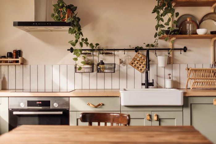 A kitchen island with a sleek marble top in the foreground, a vintage green countertop featuring drawers, pendant lights overhead, and jars filled with flowers, with a softly blurred background.