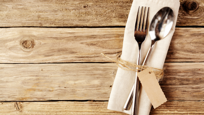 A silver spoon and fork resting on a napkin placed on a wooden table
