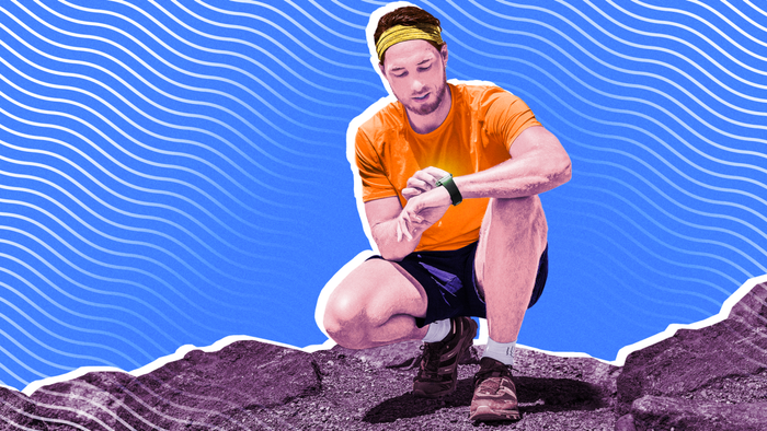 A man crouching on rugged terrain, examining his fitness device