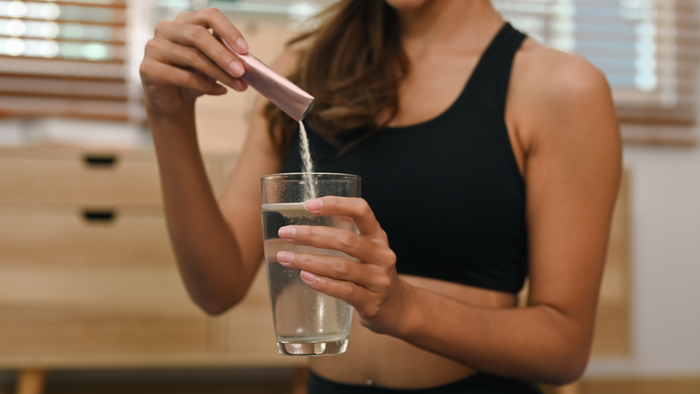 A woman stirring collagen powder into a glass of water