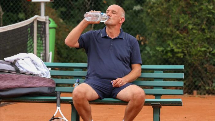 An older man relaxing on a bench, hydrating after a tennis match