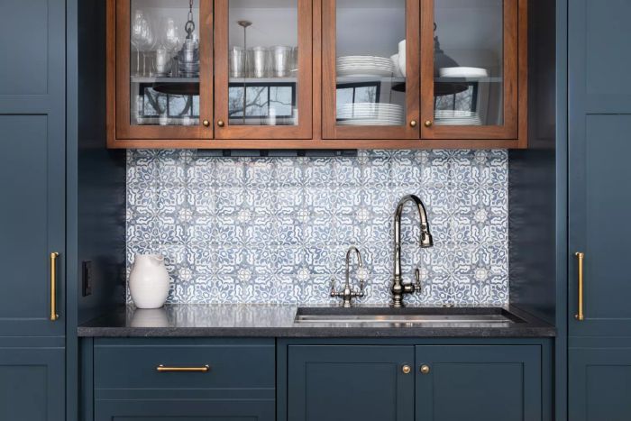 A kitchen sink paired with a tiled backsplash and framed by blue and wooden cabinets