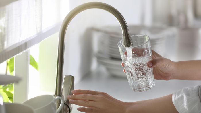 A woman pouring water into a glass from the kitchen tap