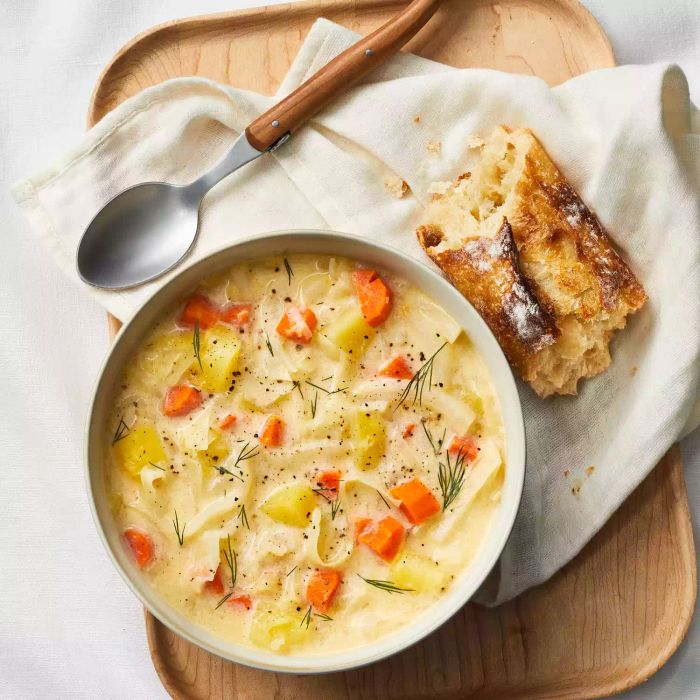 A bowl of creamy cabbage and potato soup, accompanied by a spoon and a slice of toasted bread.
