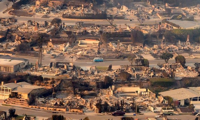 Aerial shot of a neighborhood showing severe destruction, with a solitary blue van resting on the road amidst the wreckage.