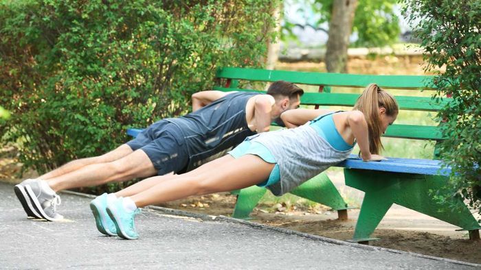 individuals performing pushups on a park bench