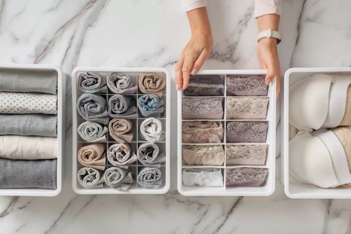 A woman's hands neatly arranging drawer organizers filled with folded underwear and socks. A perfectly organized sock drawer, showcasing a tidy collection of clothes.