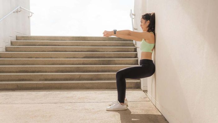 A female athlete performs a wall sit against a rugged stone surface