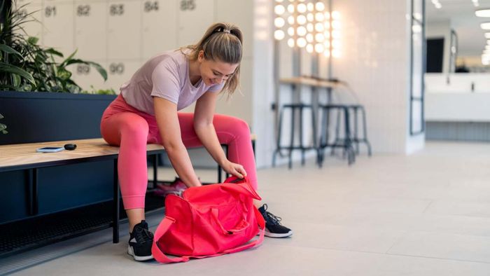 A woman on a gym bench, sifting through her pink workout bag