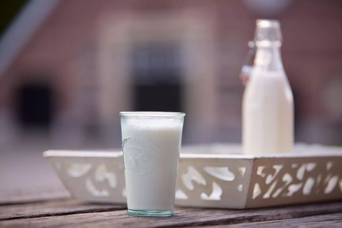 A full glass of milk rests on a white tray beside a nearly full bottle of milk.
