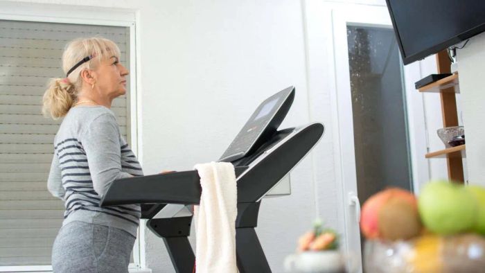 A woman dressed in comfy workout clothes walks on a treadmill while enjoying her favorite TV show.