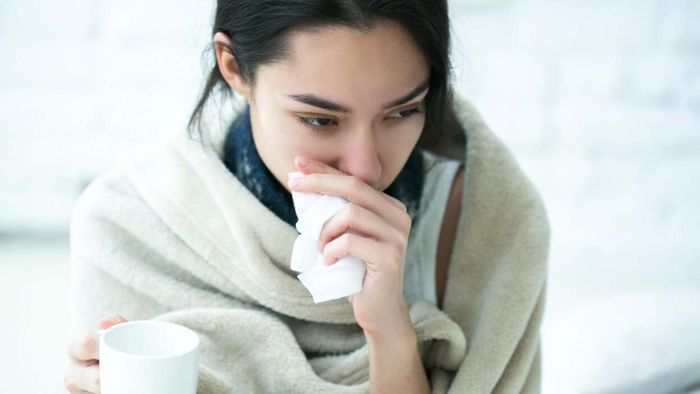 A fatigued woman bundled in a blanket, appearing visibly drained