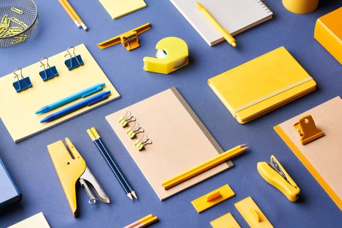 A top view of various colorful office and school supplies meticulously arranged on a blue table