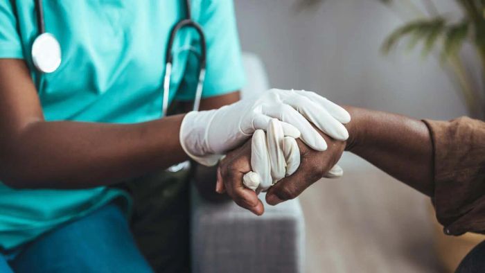 A doctor, wearing gloves, gently holds a patient's hands.