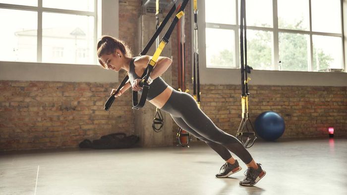 A person performing a pushup using a TRX suspension trainer in a gym environment